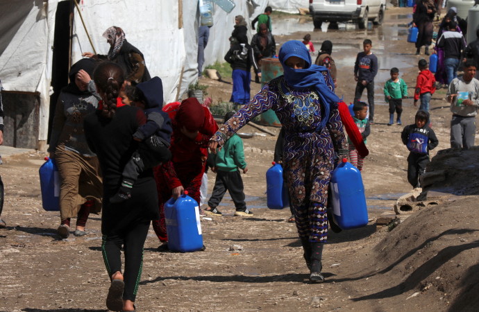 Syrian refugees walk as they carry containers at an informal tented settlement in the Bekaa valley, Lebanon March 12, 2021. (Credit: REUTERS/MOHAMED AZAKIR) 