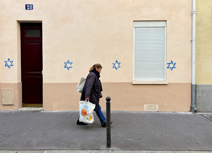 A woman walks past a building tagged with Stars of David in Paris, France, October 31, 2023 (Credit: REUTERS/LUCIEN LIBERT)