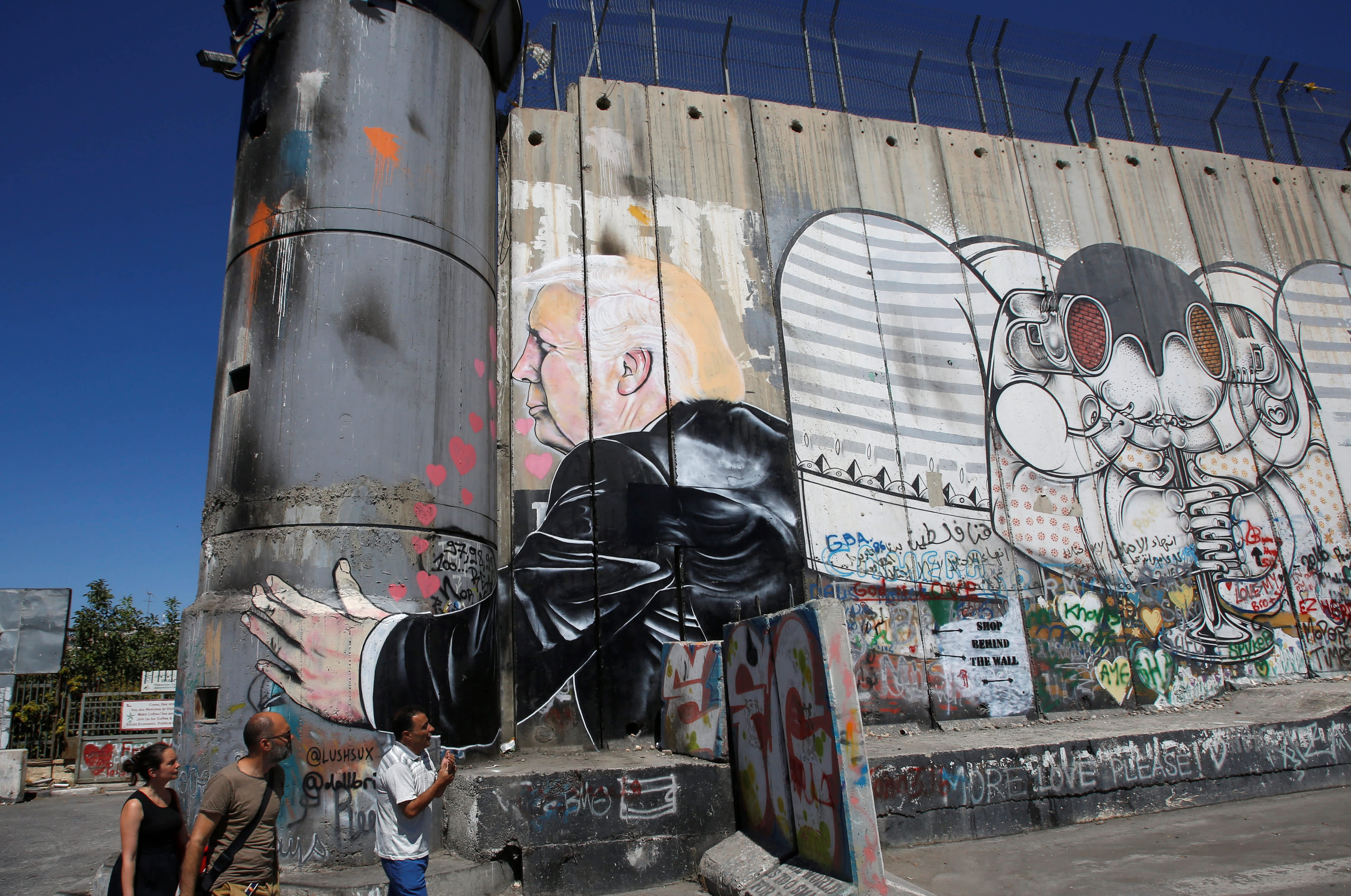Tourists stand in front of a grafitti depicting US President Donald Trump on the controversial Israeli barrier in the West Bank town of Bethlehem August 4, 2017. 