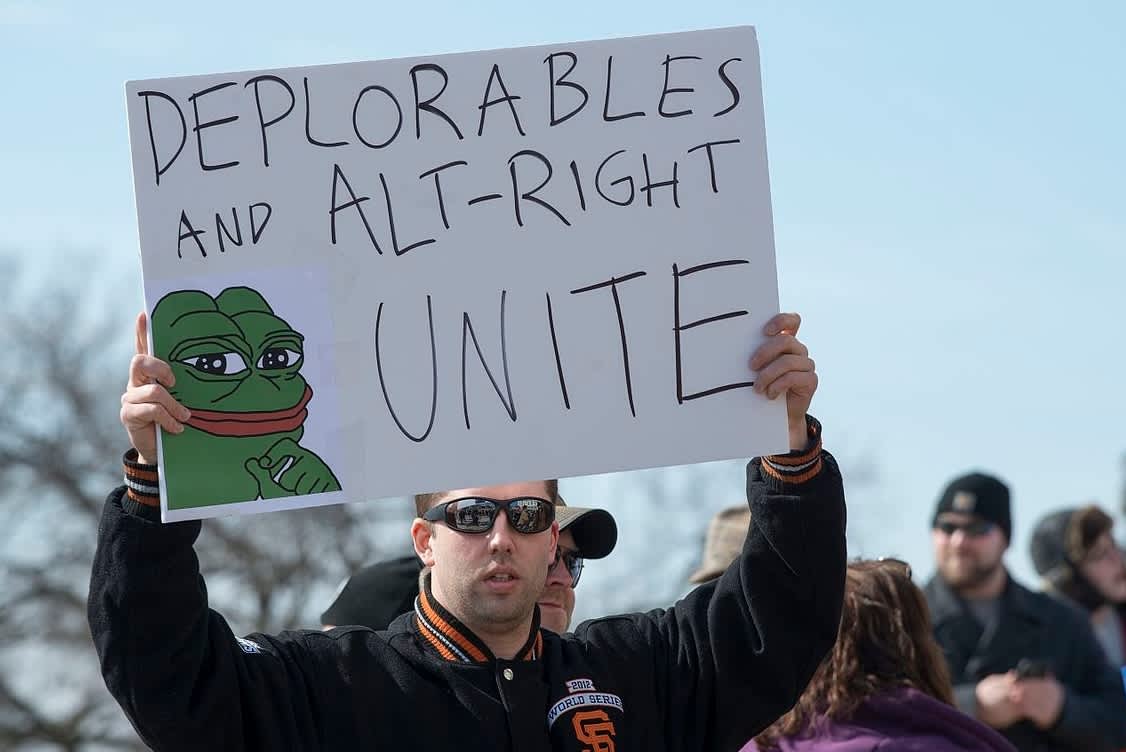 An alt-right protestor holds a sign depicting Pepe the Frog