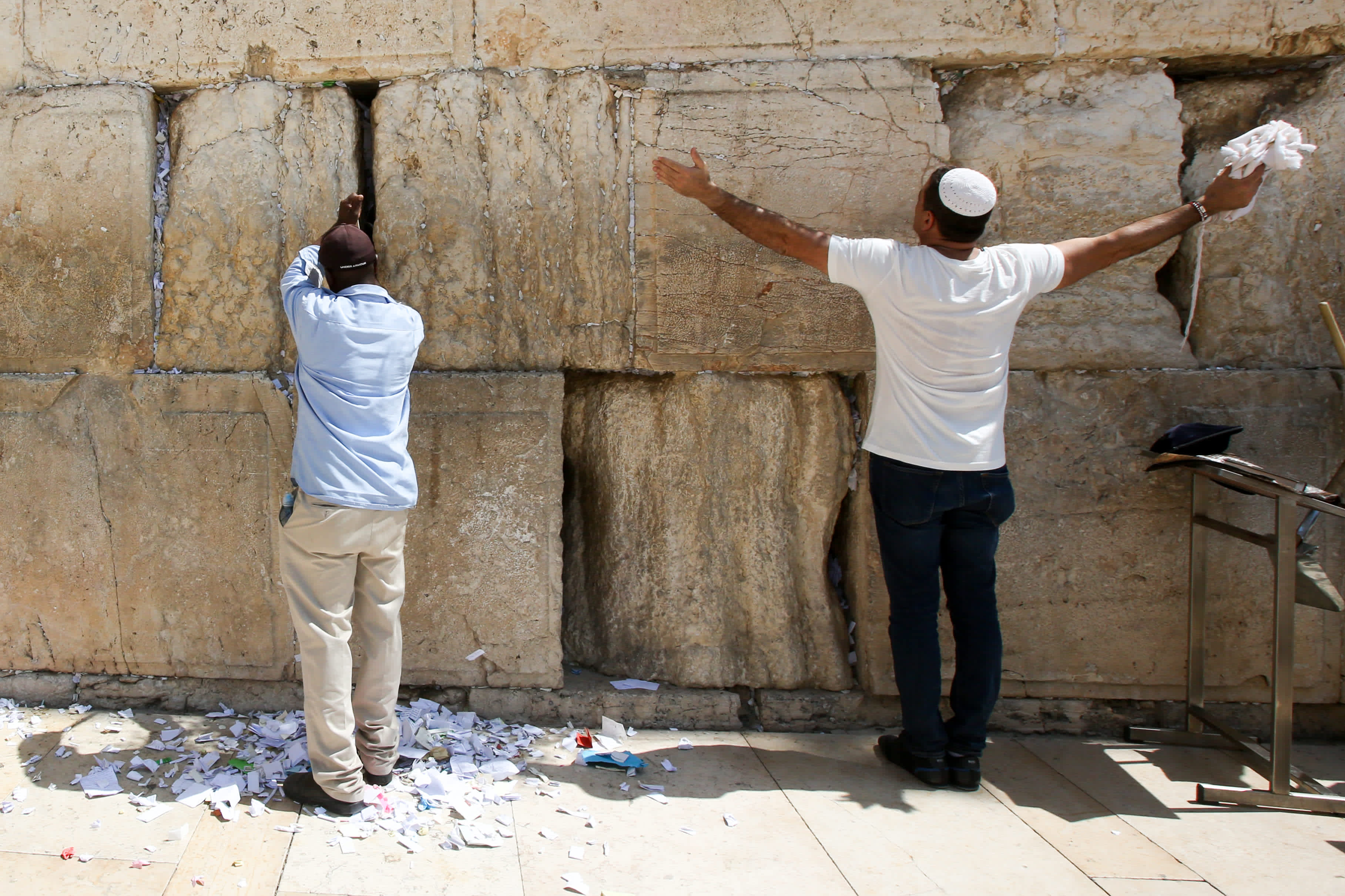 Man prays while another cleans out Western Wall notes