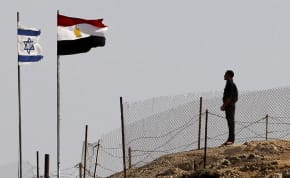  An Egyptian soldier stands near the Egyptian national flag and the Israeli flag at the Taba crossing between Egypt and Israel, about 430 km (256 miles) northeast of Cairo, October 26, 2011
