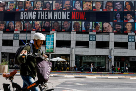  A man pushes a bike near a billboard with pictures of hostages kidnapped in the deadly October 7 attack on Israel by the Palestinian Islamist group Hamas from Gaza, in Tel Aviv, Israel March 18, 2024. 