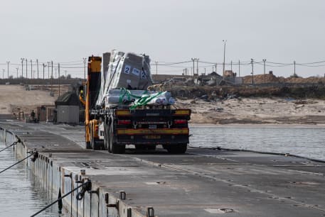 Trucks deliver humanitarian aid over a temporary pier on the Gaza coast, May 18, 2024