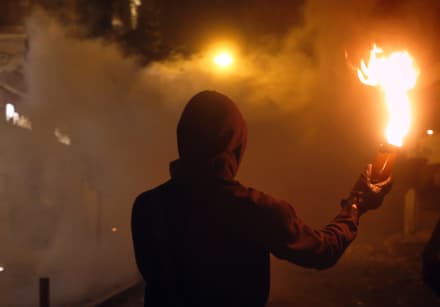 Hooded man holds flaming Molotov cocktail