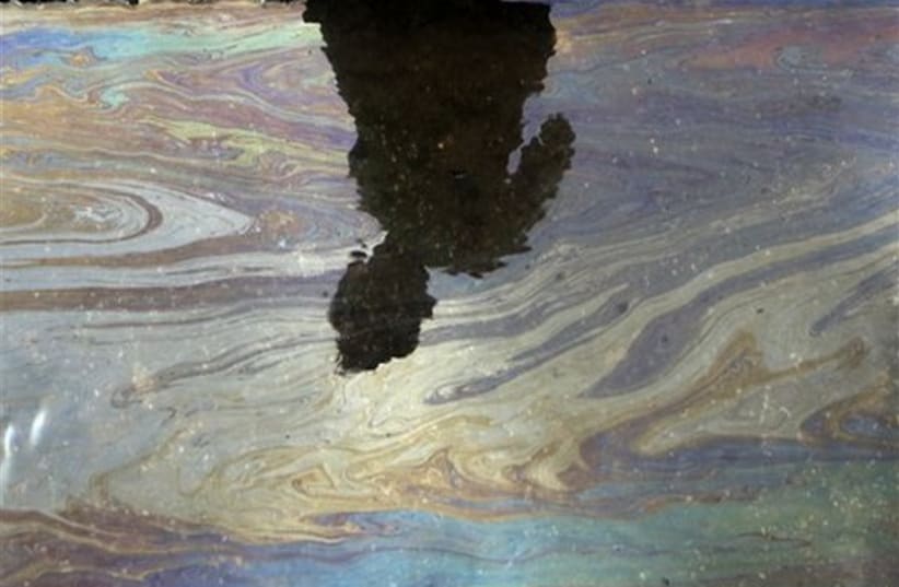 A boy casts a shadow on the water contaminated with oil near (photo credit: AP)