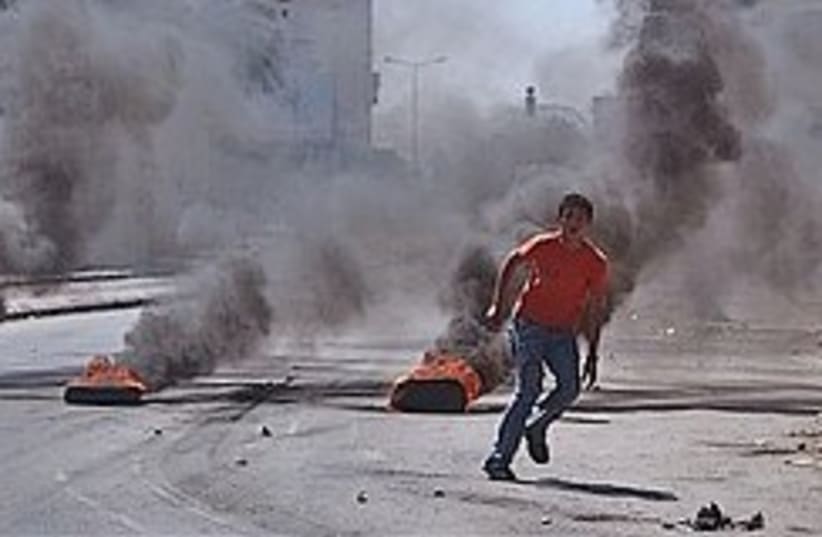 A Palestinian youth runs next to burning tires during IDF operations in Nablus. (photo credit: AP)
