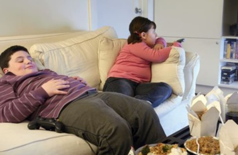 Overweight brother and sister sitting on a sofa (photo credit: Thinkstock/Imagebank)