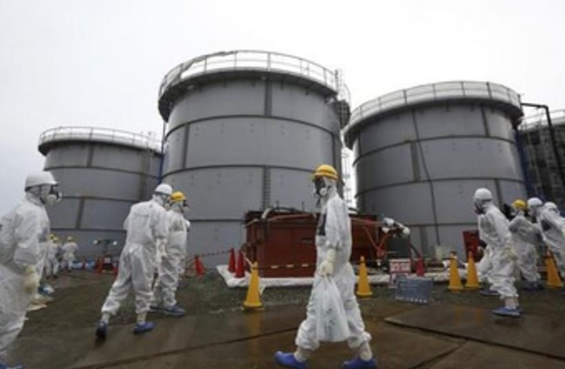 Employees wearing protective suits and masks walk past storage tanks for radioactive water  (photo credit: REUTERS)