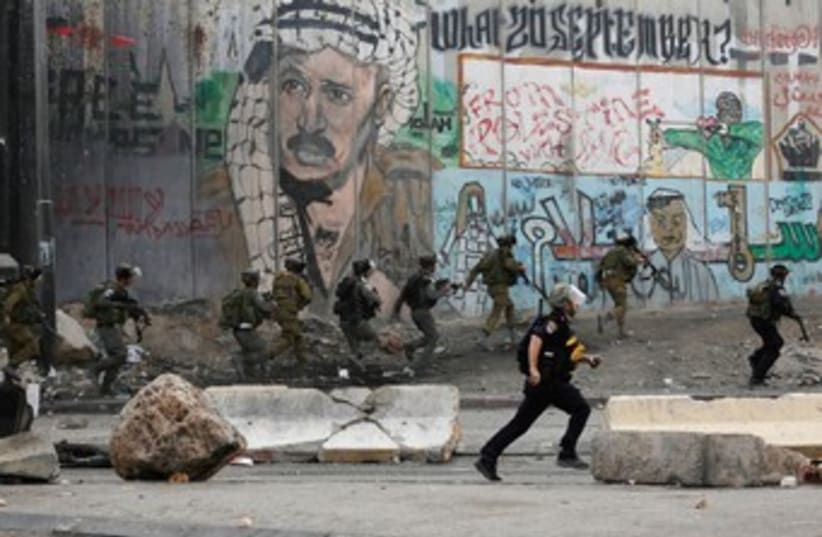 Soldiers and border policemen run past a section of the West Bank security barrier. (photo credit: REUTERS)