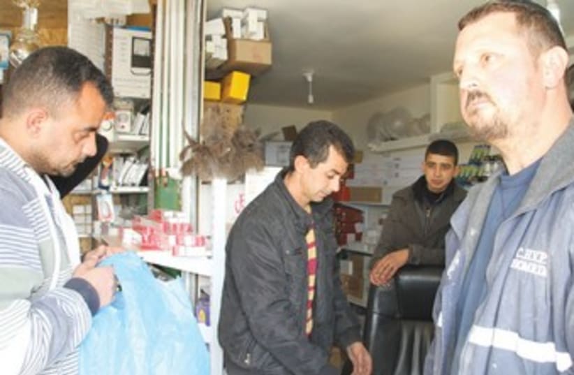 RELIGIOUS SETTLER Yanki Herchkov (right) shops last week in the store that Mustafa Sabateen (center) owns in the West Bank Palestinian village of Husan. (photo credit: TOVAH LAZAROFF)