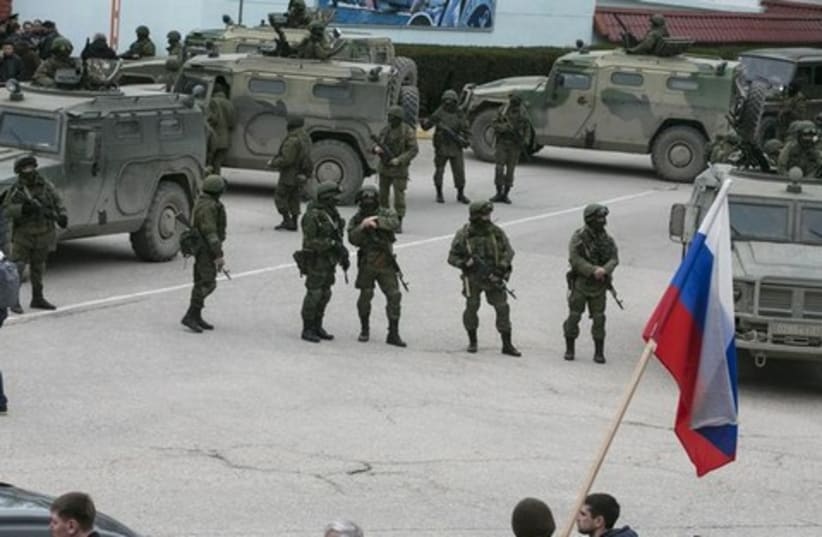 Pro-Russian men hold Russian flags in front of armed servicemen near Russian army vehicles outside a Ukrainian border guard post in the Crimean town of Balaclava March 1, 2014.  (photo credit: REUTERS/BAZ RATNER)