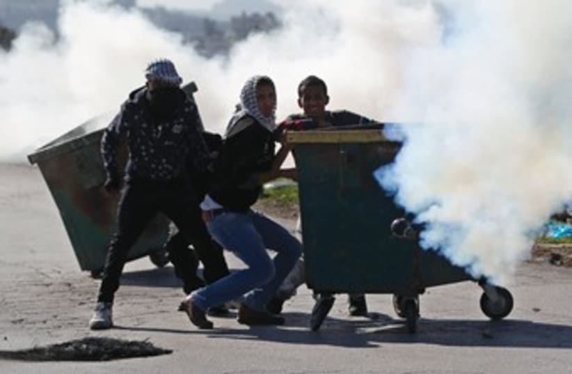 Stone-throwing Palestinian protesters take cover behind a garbage bin amidst tear gas fired by Israeli troops during clashes at a checkpoint near Ramallah last month. (photo credit: REUTERS)