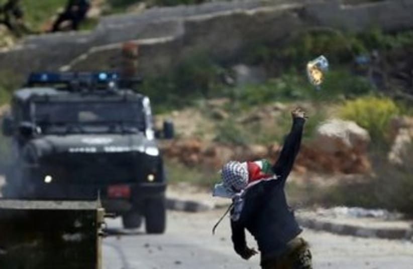 A Palestinian protester throws a Molotov cocktail towards a Border Police jeep during clashes outside the Ofer military prison near Ramallah, April 4, 2014. (photo credit: REUTERS)