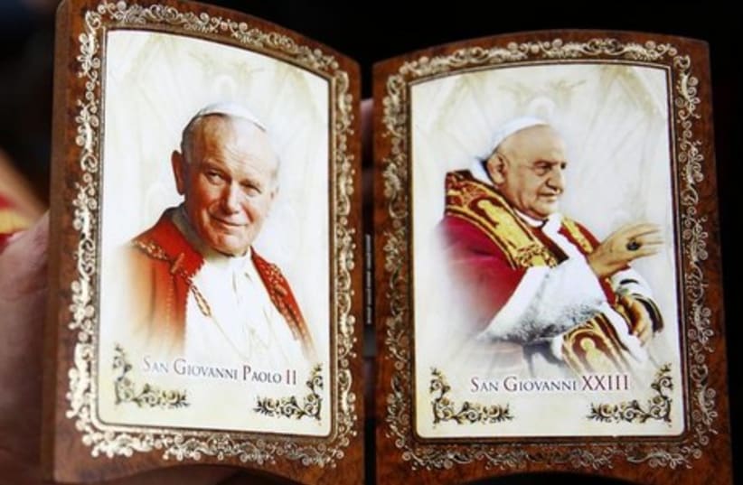 A Polish pilgrim displays a souvenir of canonized Popes John Paul II (L) and John XXIII while waiting for mass before the canonization ceremony in St Peter's Square at the Vatican, April 27, 2014. (photo credit: REUTERS)