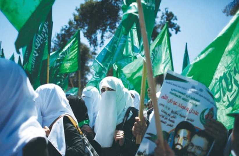 Women hold Hamas flags as they take part in the funeral of leading Hamas terrorists Imad and Adel Awadallah last month. (photo credit: REUTERS)