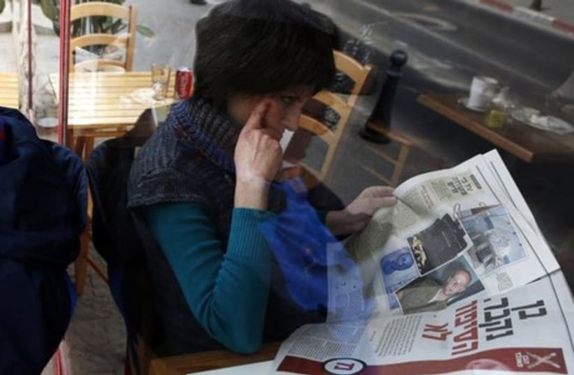 A woman is seen through a coffee shop window as she reads an article about Ben Zygier in an Yedioth Ahronoth newspaper in Jerusalem, February 15, 2013. (photo credit: REUTERS)