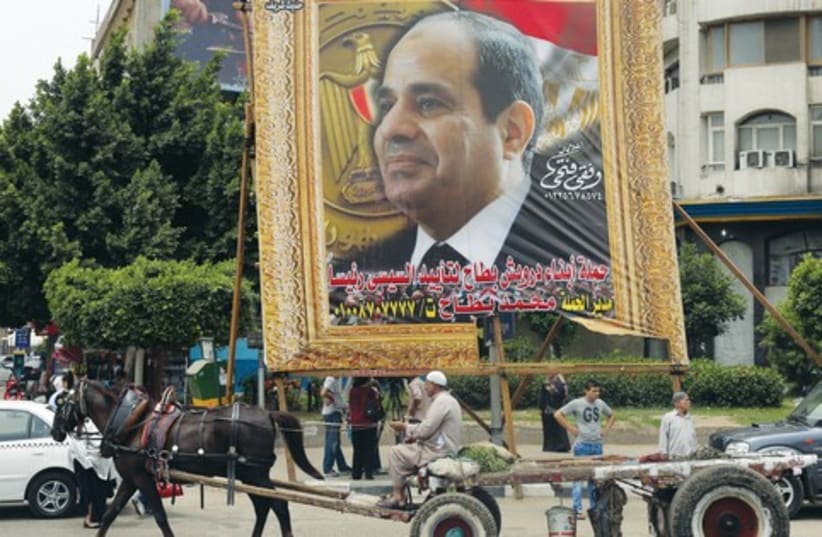 Man on a horse-drawn cart rides past banner depicting  Abdel Fattah al-Sisi in Cairo (photo credit: REUTERS)