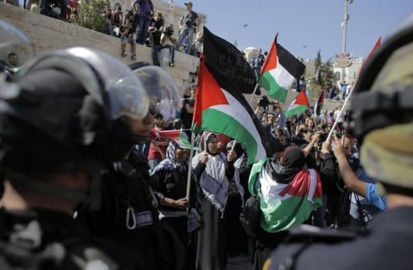 Palestinian protesters wave flags as Israeli policemen guard nearby during a demonstration marking Nakba Day. (photo credit: REUTERS)