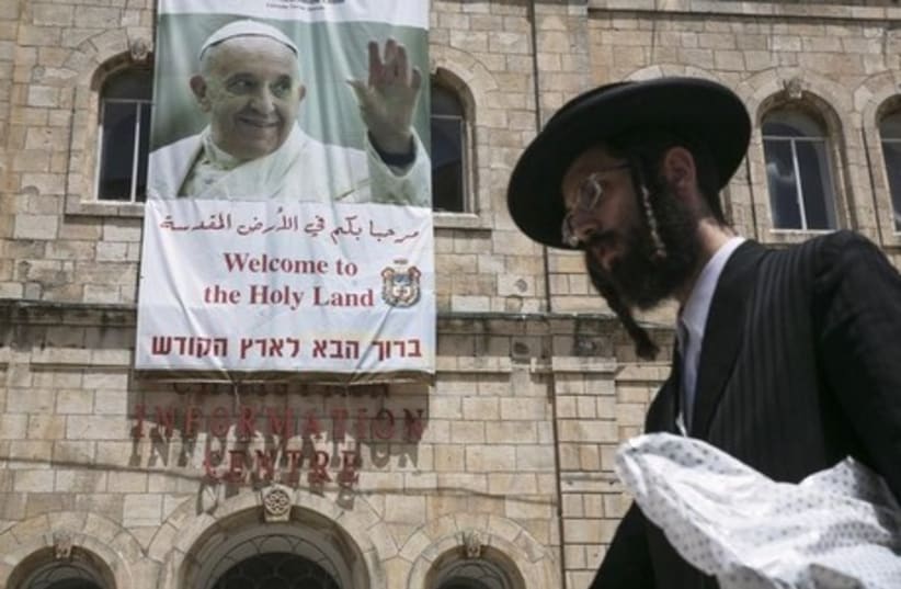 An ultra-Orthodox Jewish man walks past a banner depicting Pope Francis, in Jerusalem's Old City (photo credit: REUTERS)