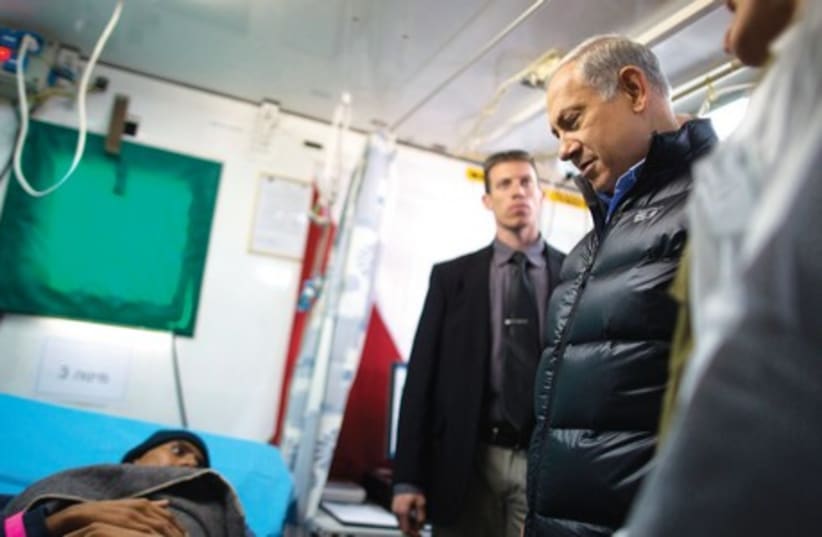 Prime Minister Benjamin Netanyahu speaks to an injured Syrian man being treated by the IDF (photo credit: MENAHEM KAHANA / REUTERS)