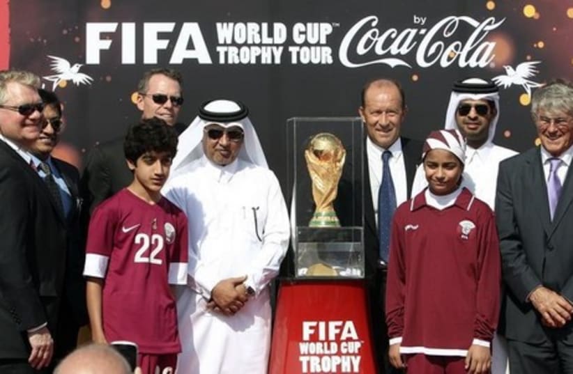 Qatari soccer officials pose with others next to the FIFA World Cup trophy following its arrival in Doha (photo credit: REUTERS)