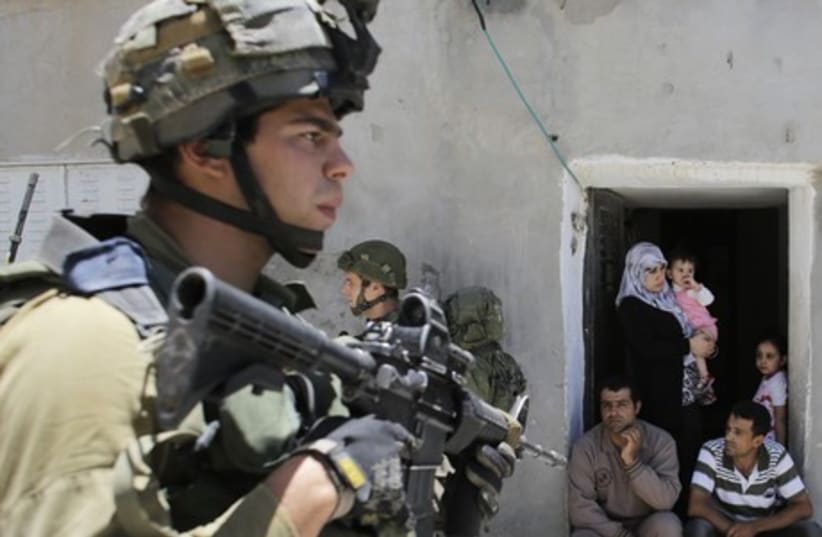 Palestinians sit outside their house as Israeli soldiers patrol near the West Bank City of Hebron June 15, 2014. (photo credit: REUTERS)