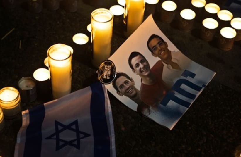 Candles placed next to a picture of three Israeli teenagers who were abducted and killed, in Tel Aviv's Rabin Square June 30, 2014. (photo credit: REUTERS)