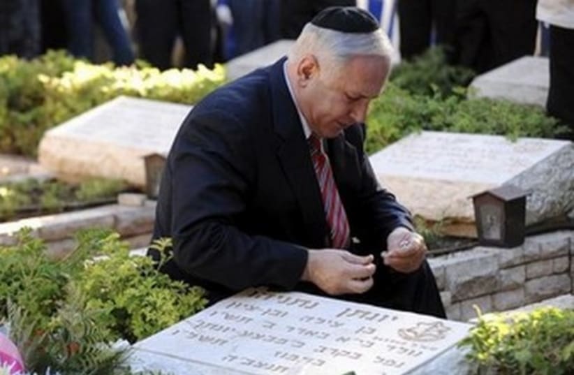 Prime Minister Binyamin Netanyahu kneels at the gravesite of his brother, Yoni Netanyahu. (photo credit: REUTERS)