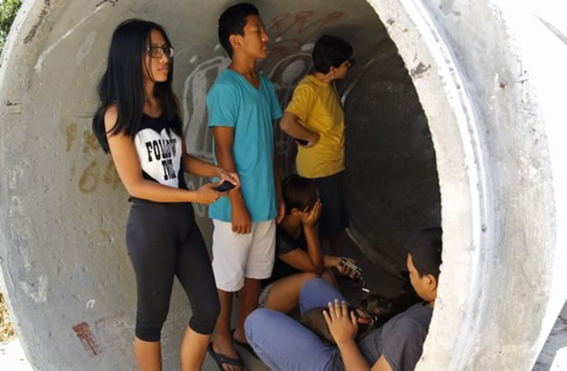 Residents take cover in a concrete pipe as a siren warning of incoming rockets is sounded near Ashdod (photo credit: REUTERS)
