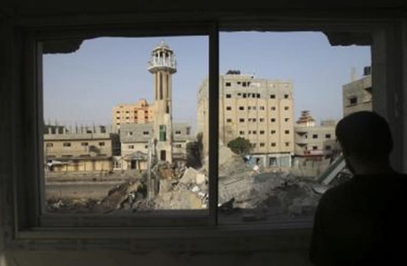 A Palestinian man looks through a broken window in the Gaza Strip, which police said was destroyed in an IAF strike. (photo credit: REUTERS)
