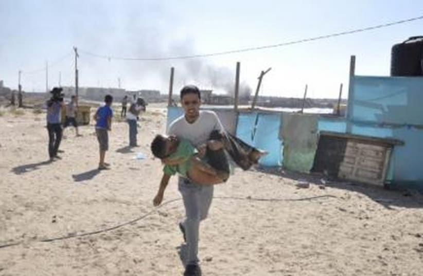 Man carries child on Gaza beach after Navy shelling (photo credit: REUTERS)