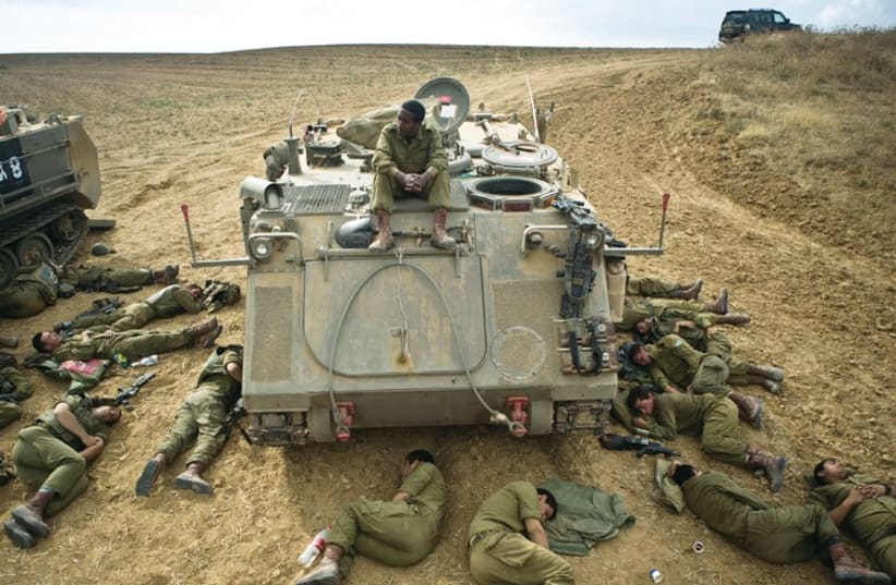 IDF SOLDIERS sleep on the ground next to an armored personnel carrier outside the Gaza Strip. (photo credit: REUTERS)