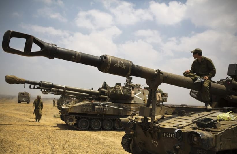 An Israeli soldier sits atop a mobile artillery unit in a staging area outside the Gaza Strip (photo credit: REUTERS)