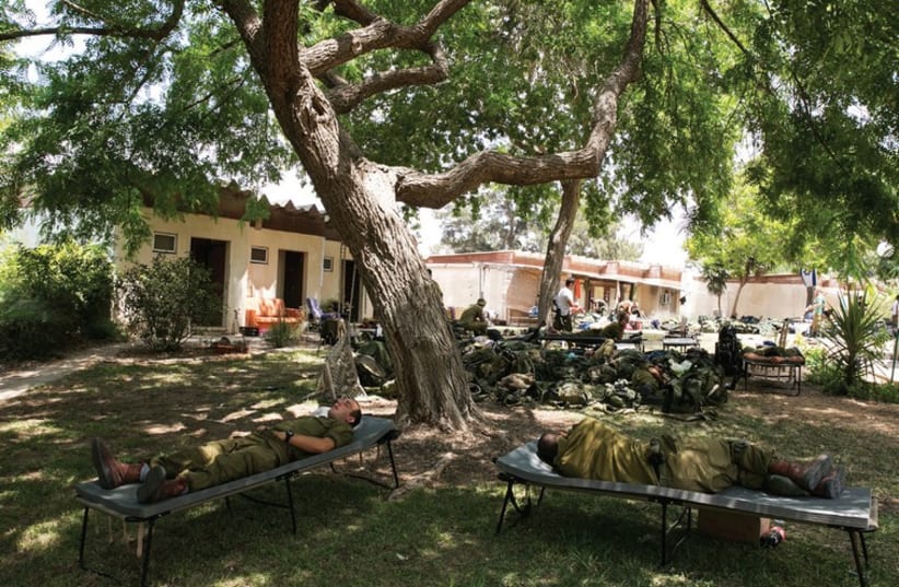 Soldier camp out last month on the lawn in Kibbutz Nir Am, just outside the Gaza Strip. (photo credit: REUTERS)