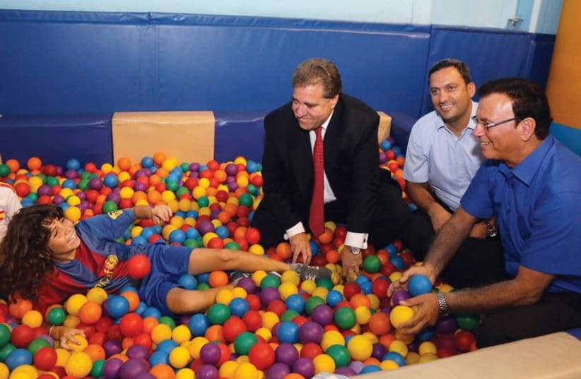 Left to right: KKL-JNF US Chairman Russell Robinson, Sderot Mayor Alon Davidi and KKL-JNF chairman Efi Stenzler with children in a protected indoor playground in Sderot. (photo credit: ADI YISRAEL)