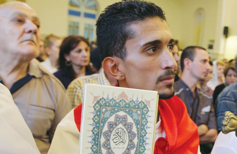An Iraqi man carrying a Koran and a cross attends mass at Mar Girgis Church in Baghdad on July 20 (photo credit: REUTERS)