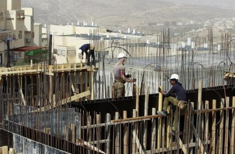 Palestinian laborers work on a construction site in a religious Jewish settlement in the West Bank. [File] (photo credit: REUTERS)