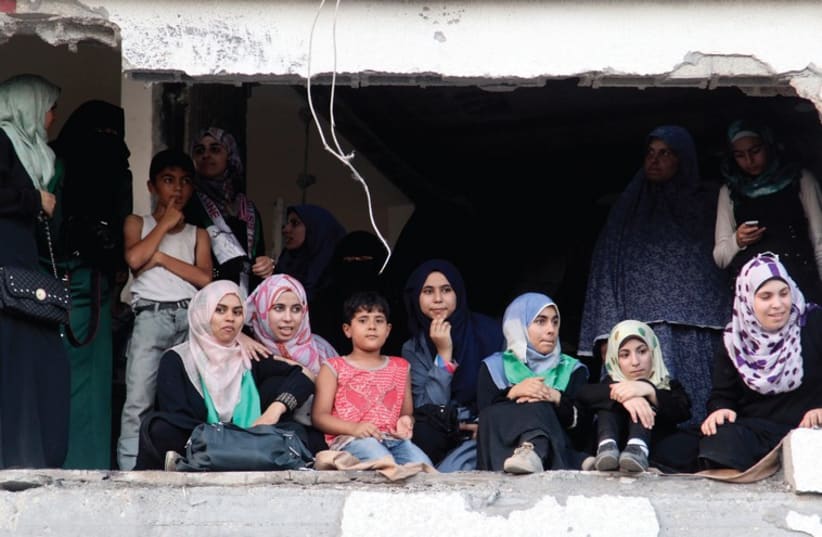 PALESTINIANS SIT in a damaged house as they watch a parade celebrating Hamas’s ‘victory’ over Israel, in the Shejaia neighborhood, Gaza (photo credit: REUTERS)