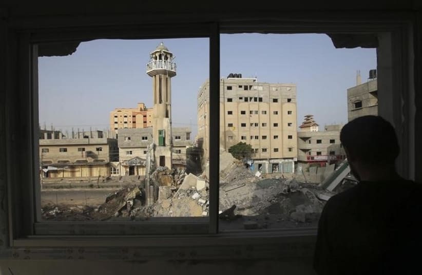 A Palestinian man looks through a broken window at the rubble of a mosque, which police said was destroyed in an Israeli air strike, in the central Gaza Strip July 12, 2014.  (photo credit: REUTERS)