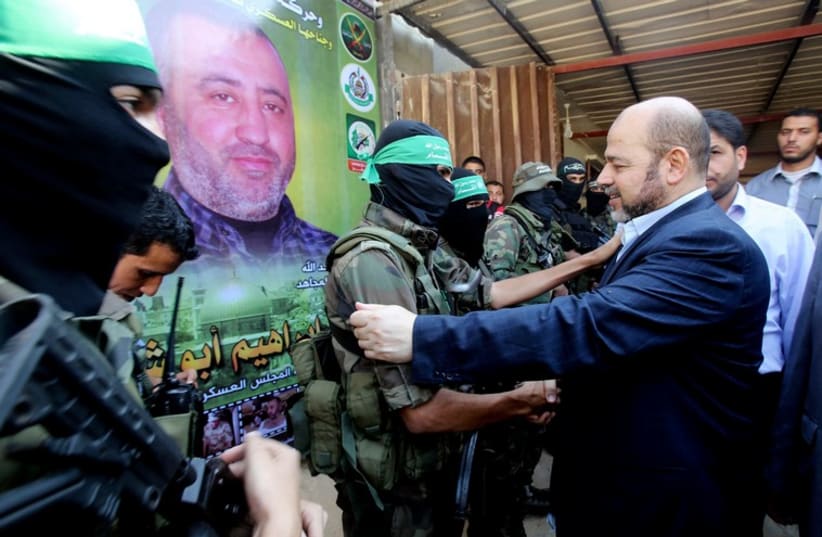 Hamas political leader Musa Abu Marzouk (R) shakes hands with a Hamas militant as he visits the mourning tent of senior Hamas commander Mohammed Abu Shammala (seen in posters). (photo credit: REUTERS)