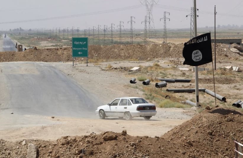 A car drives near a flag belonging to Islamic State militants at the end of a bridge in southern Kirkuk (photo credit: REUTERS)