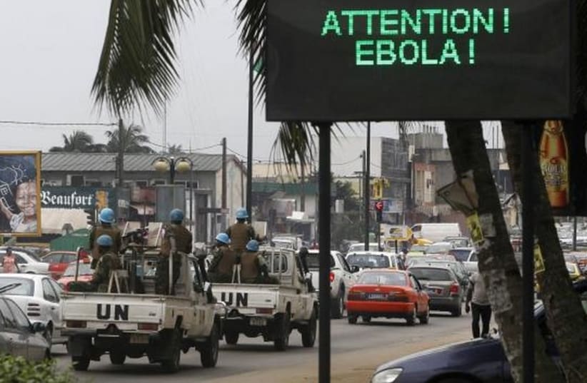 A UN convoy of soldiers passes a screen displaying a message on Ebola on a street in Abidjan. (photo credit: REUTERS)