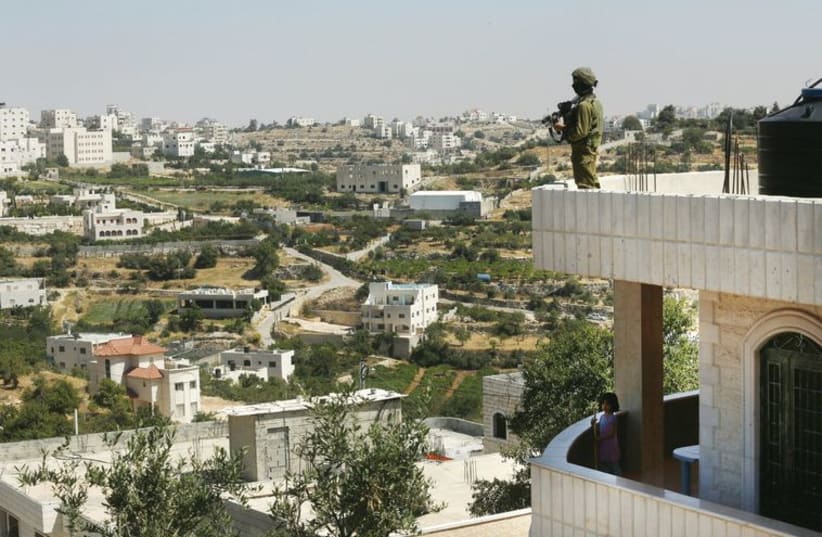 A soldier stands guard on a house in Hebron on June 18, during Operation Brother’s Keeper. (photo credit: MARC ISRAEL SELLEM/THE JERUSALEM POST)