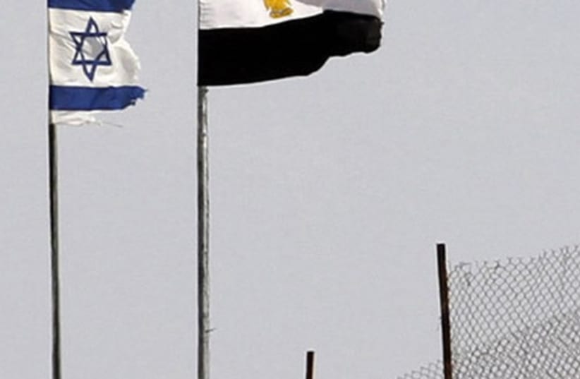 An Egyptian soldier stands near the Egyptian national flag and the Israeli flag at the Taba crossing between Egypt and Israel (photo credit: REUTERS)