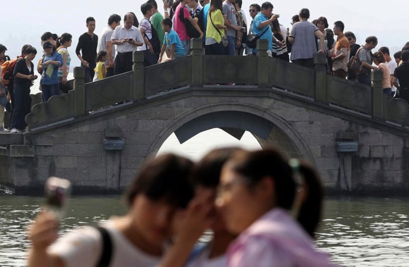 Three women pose for a selfie as tourists crowd on a bridge above the West Lake, on the third day of the seven-day national holiday in Hangzhou, Zhejiang province  (photo credit: REUTERS)