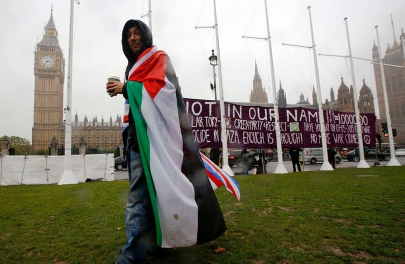 A pro-Palestinian supporter wears a Palestinian and Union flag outside the Houses of Parliament in London.  (photo credit: REUTERS)