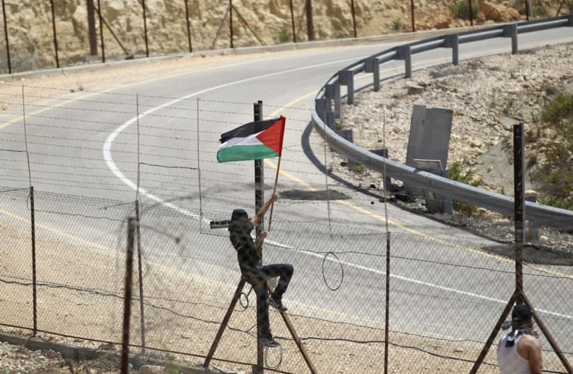 A protester places a Palestinian flag at the Israeli barrier fence in the West Bank village of Rafat near Ramallah (photo credit: REUTERS)