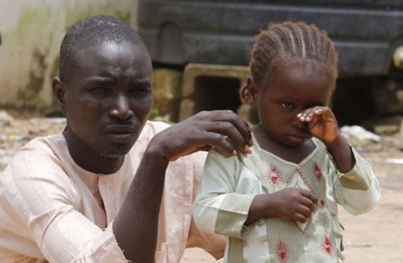 A girl rubs her eye beside her father in an internally displaced persons (IDP) camp, that was set up for Nigerians fleeing the violence committed against them by Boko Haram militants (photo credit: REUTERS)