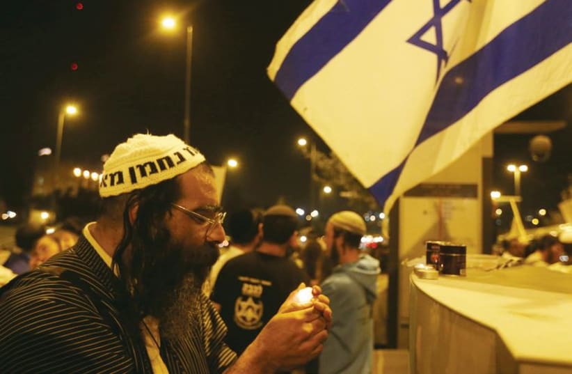 A man lights a candle at a makeshift memorial for the victims of the October 22 terrorist attack at the Ammunition Hill light rail stop in Jerusalem. (photo credit: MARC ISRAEL SELLEM/THE JERUSALEM POST)